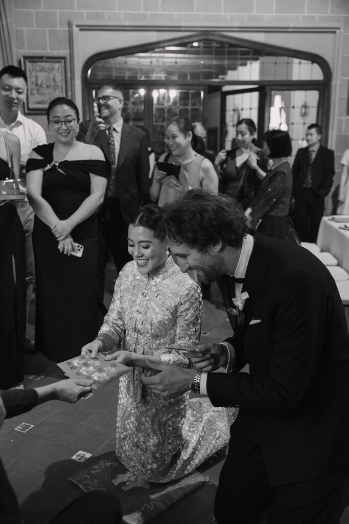 Pareja realizando la ceremonia del té china en La Baronía: novia con qipao dorado arrodillada junto al novio con esmoquin, sosteniendo tazas rojas de la tradición nupcial china
